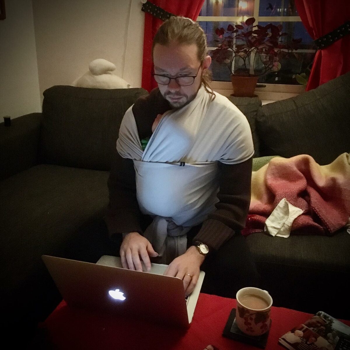 Emanuel med bebis i sjal på bröstet sitter och skriver på en dator